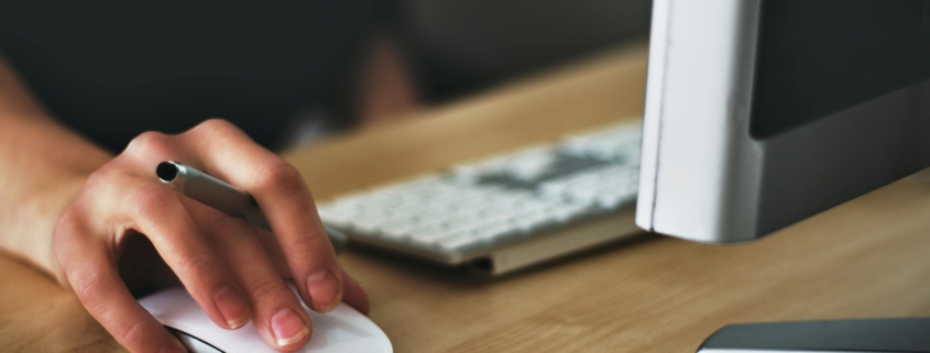 Hand auf Computermouse und aufgeklapptes Notebook